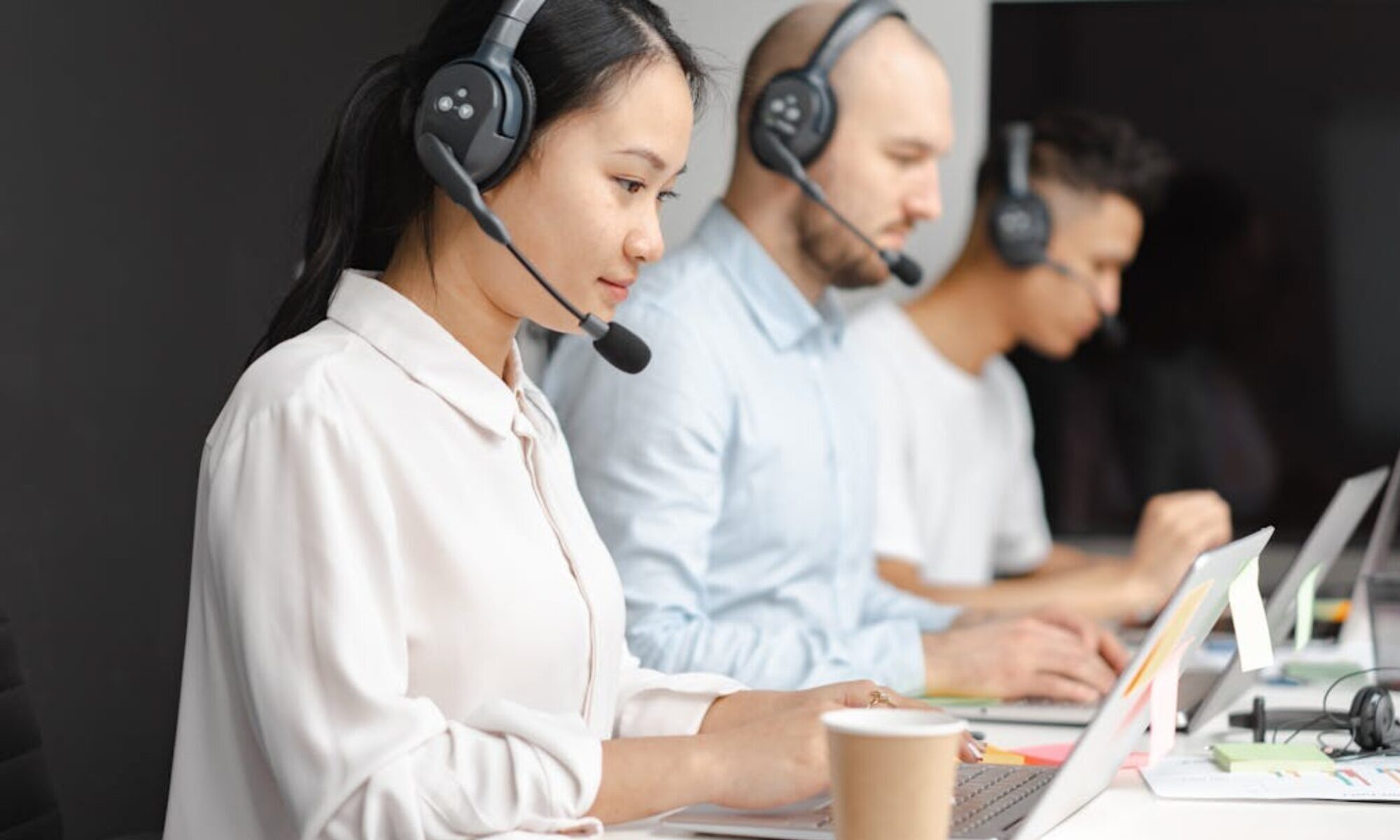 Customer service agents efficiently handle calls using laptops and headsets in a modern office.